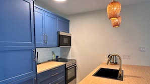 A modern kitchen with blue cabinets, a wooden countertop, a built-in oven, a microwave, and a hanging pendant light.