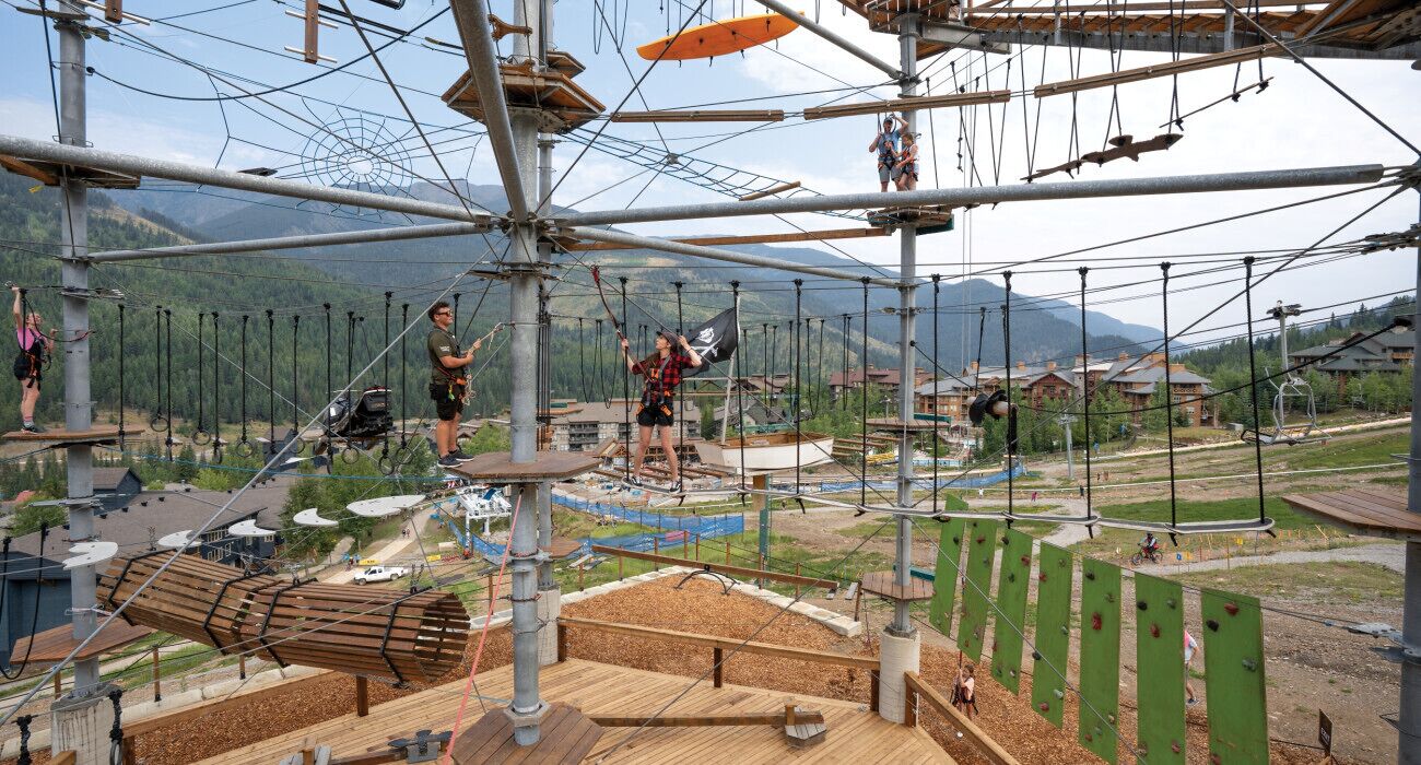 Parque de aventuras al aire libre con puentes de cuerda, paredes de escalada y un paisaje montañoso.