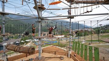Parque de aventuras al aire libre con puentes de cuerda, paredes de escalada y un paisaje montañoso.