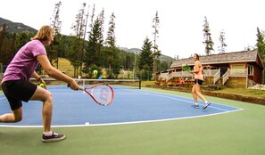 Een tennisbaan met net, omgeven door bomen en een houten hutje op de achtergrond.