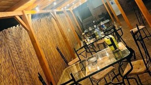 An indoor dining area with wooden ceiling beams, string lights, and a long table with chairs. - Hotel Bavaria (Craiova)