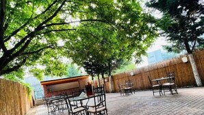 An outdoor patio area with brick flooring, metal chairs, and tables. - Hotel Bavaria (Craiova)