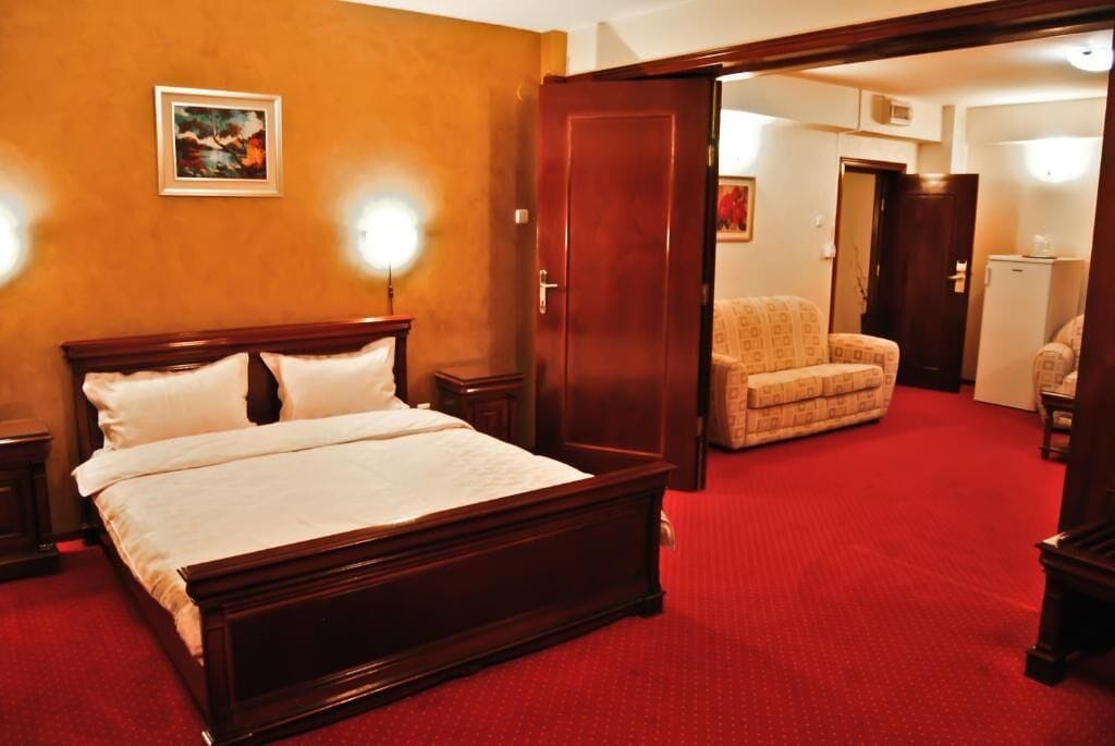Una habitación de hotel con una cama grande, una alfombra roja, una puerta de madera y una silla.