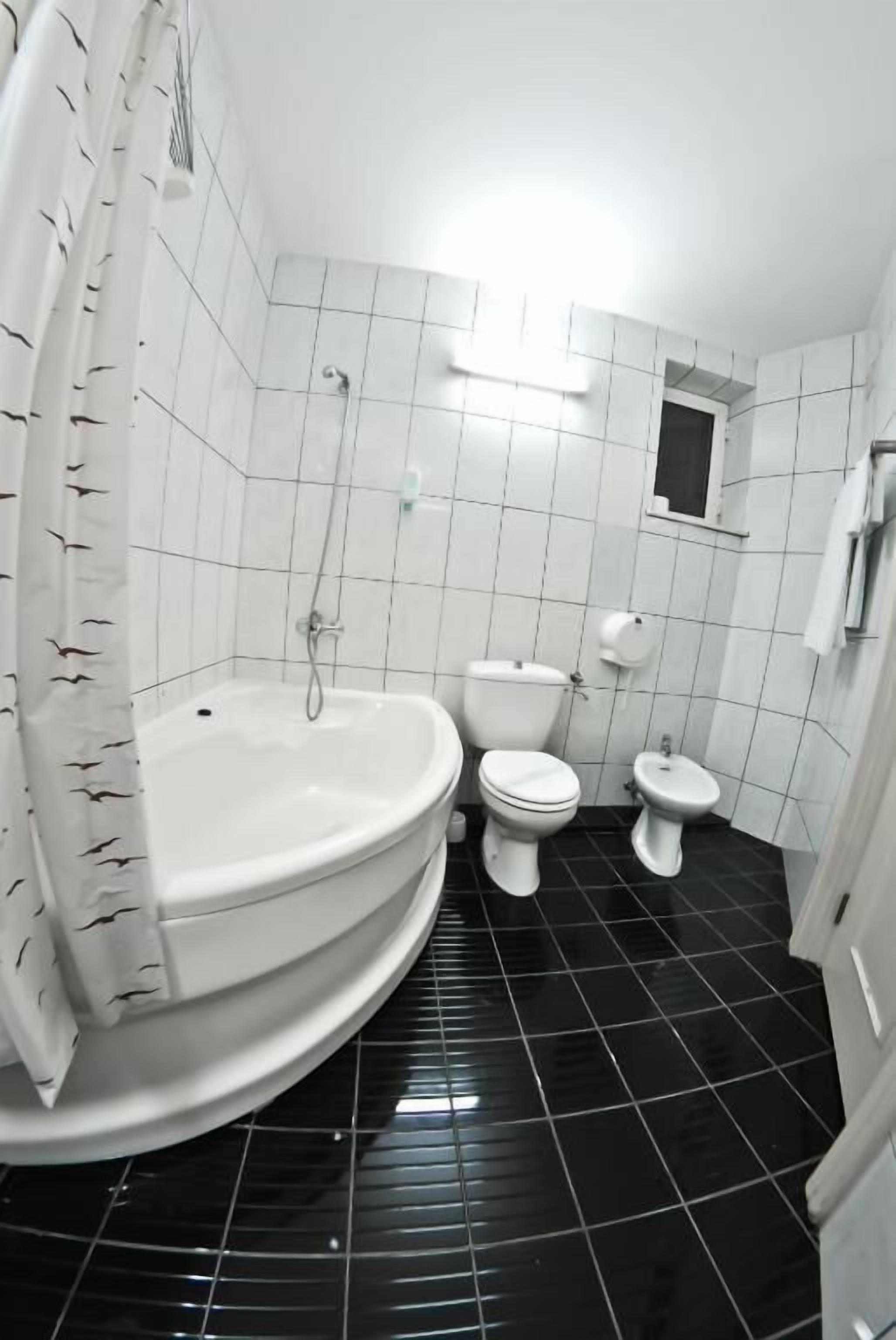 Un baño con bañera, dos inodoros y cortina de ducha.