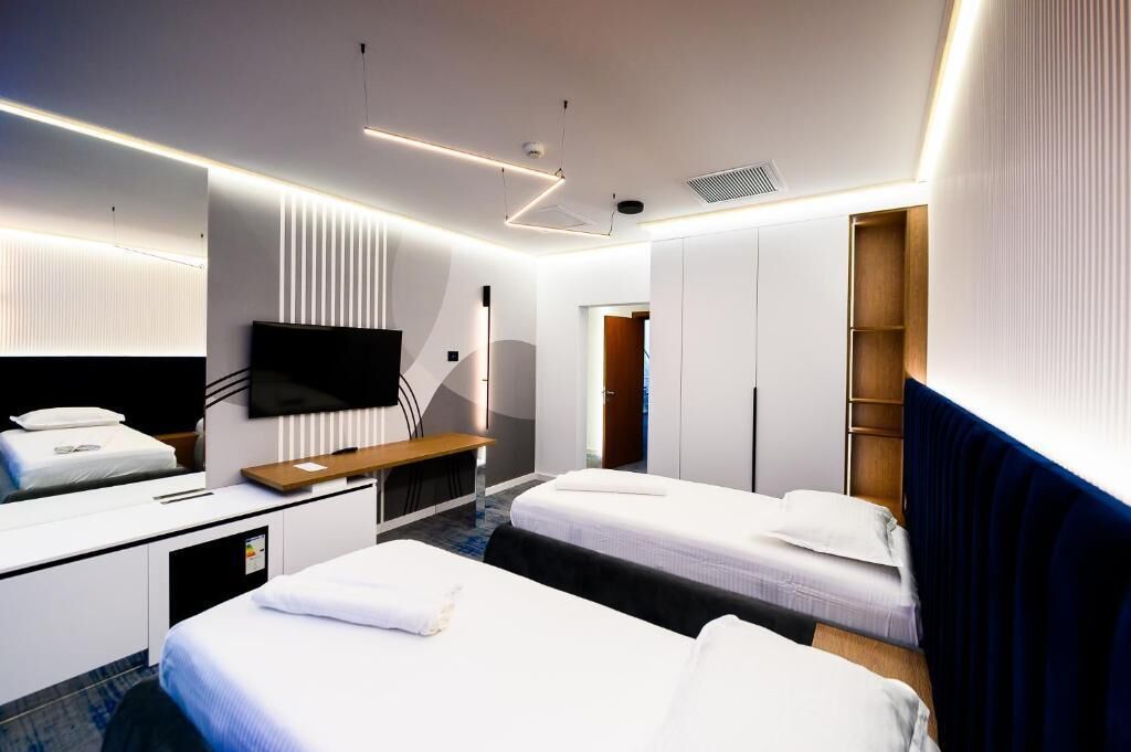 Una habitación de hotel moderna con dos camas, un escritorio, un televisor de pantalla plana y un armario.