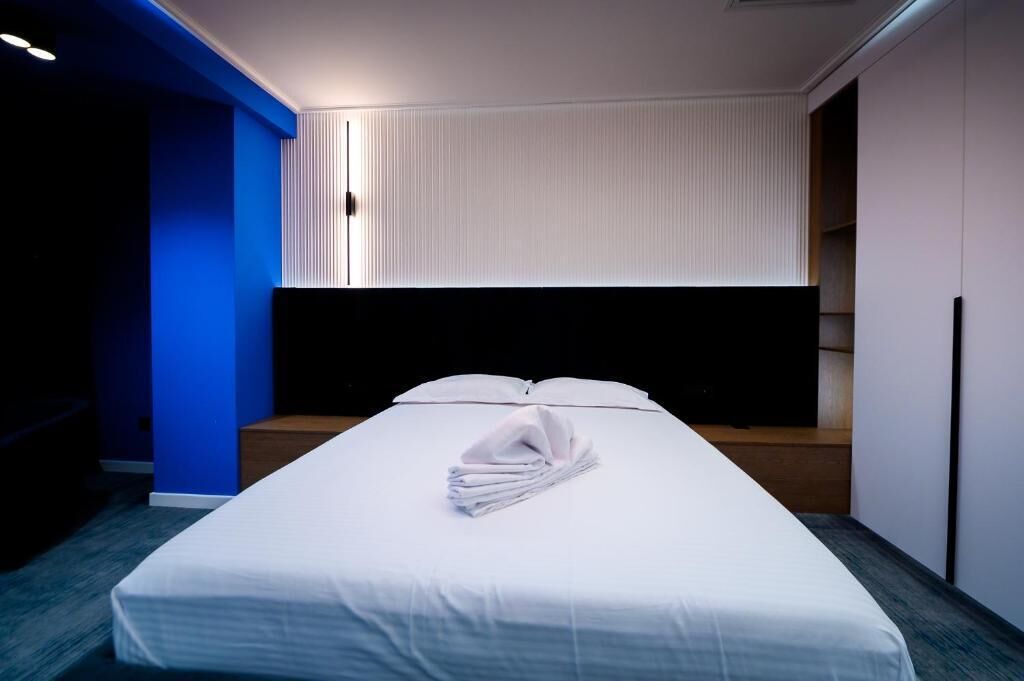 A hotel room with a bed, a nightstand, a wall-mounted TV, and a blue accent wall.