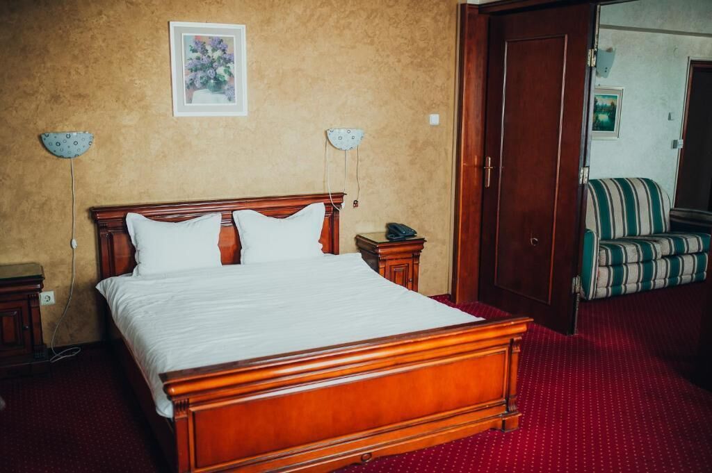 Hotellihuone, jossa on puinen sänky, yöpöytä, lamppu ja tuoli.