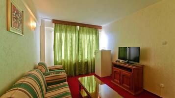 A room with a sofa, a television, a cabinet, and a refrigerator.