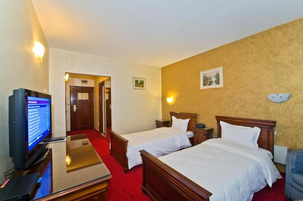 Ein Hotelzimmer mit zwei Betten, einem Fernseher, einem Schreibtisch und einem roten Teppich.
