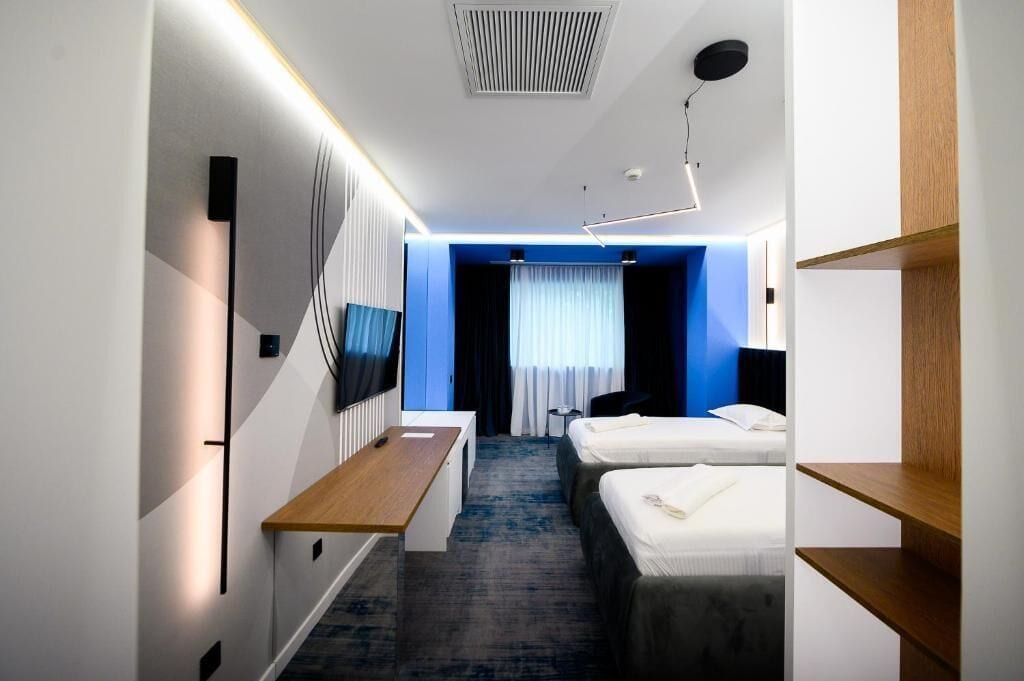 A hotel room with a desk, two beds, a TV, and a blue accent wall.