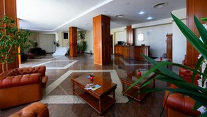 A hotel lobby with a reception desk, leather sofas, a coffee table, and a staircase leading to another floor. - Hotel Bavaria (Craiova)
