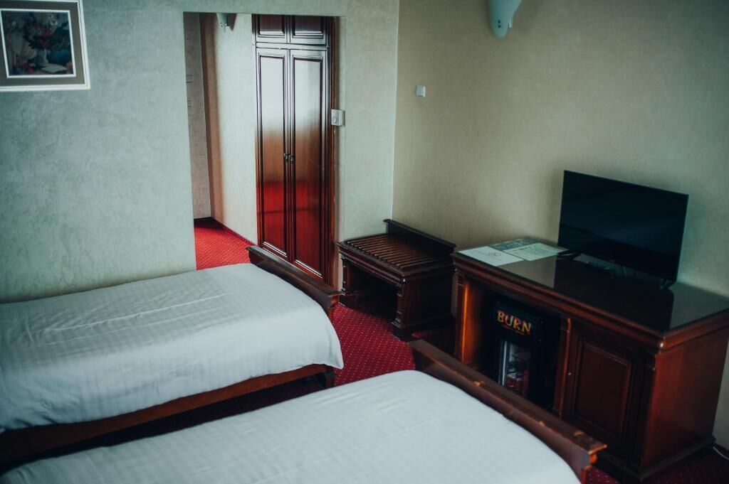 Habitación de hotel con dos camas, un televisor, un armario con un letrero que dice 'BURN' y una puerta que da a otra habitación.