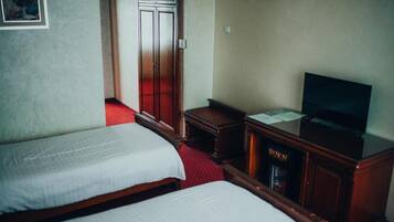 A hotel room with two beds, a television, a cabinet with a 'BURN' sign, and a door leading to another room.