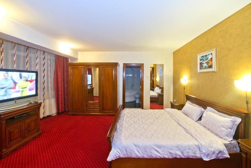 A hotel room with a large bed, a television, a wardrobe, and a bathroom visible through an open door.