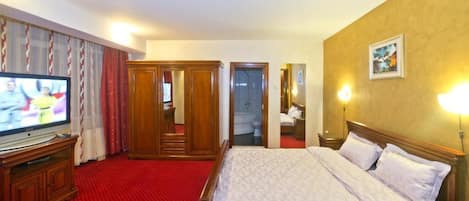 A hotel room with a large bed, a television, a wardrobe, and a bathroom visible through an open door.