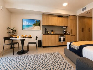 A compact hotel room with a kitchenette, a dining area, a bed, and a large window with a beach view. - Wellness Studio | Rooftop Pool & Skyline Views (Miami)