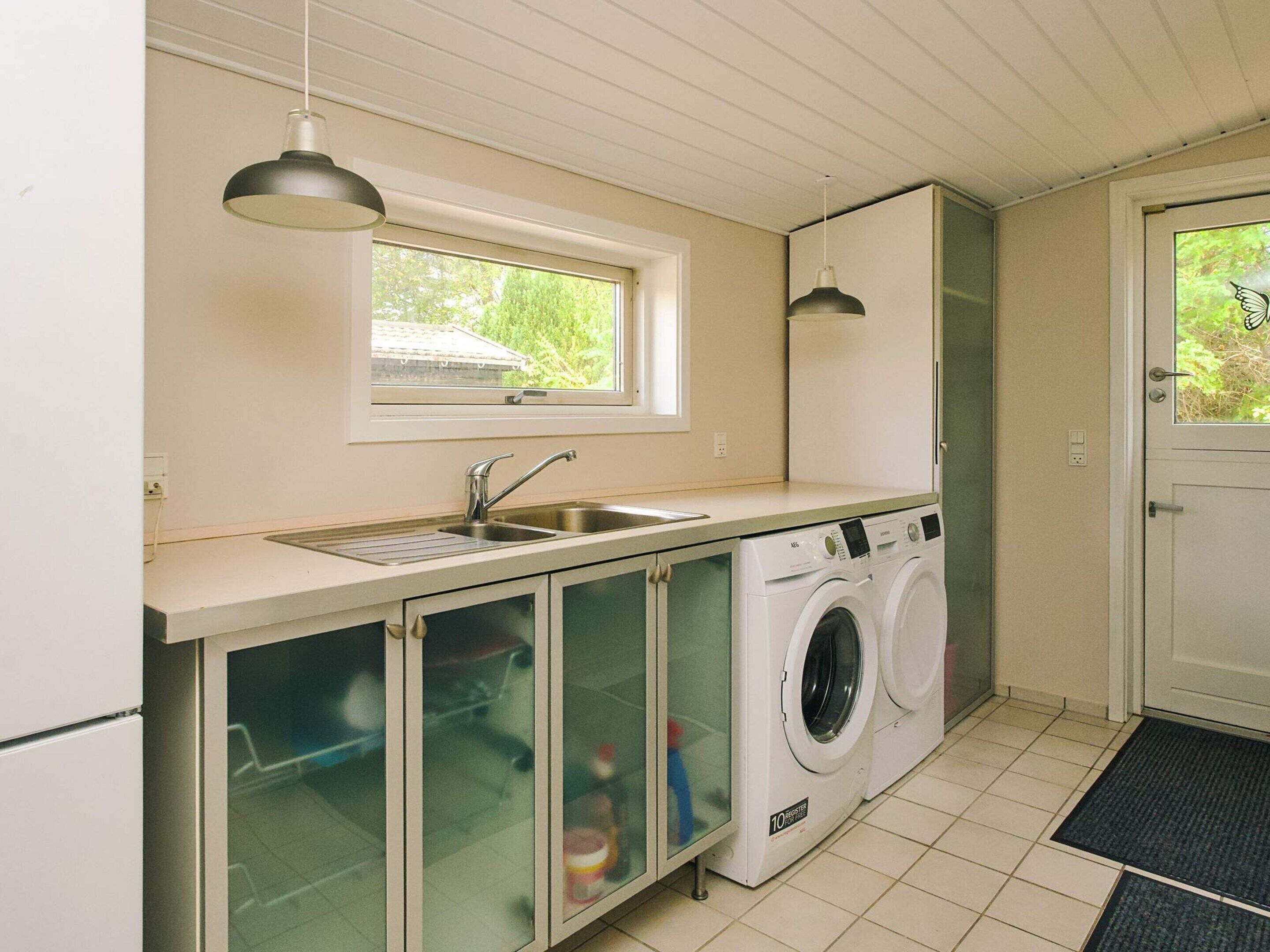 A compact kitchen with a washing machine, a sink, and a window.