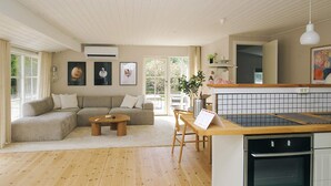 A modern living room with a sofa, a coffee table, and a kitchen area with a stove and a dining table. - 4 Star Holiday Home in Gilleleje (Gilleleje)
