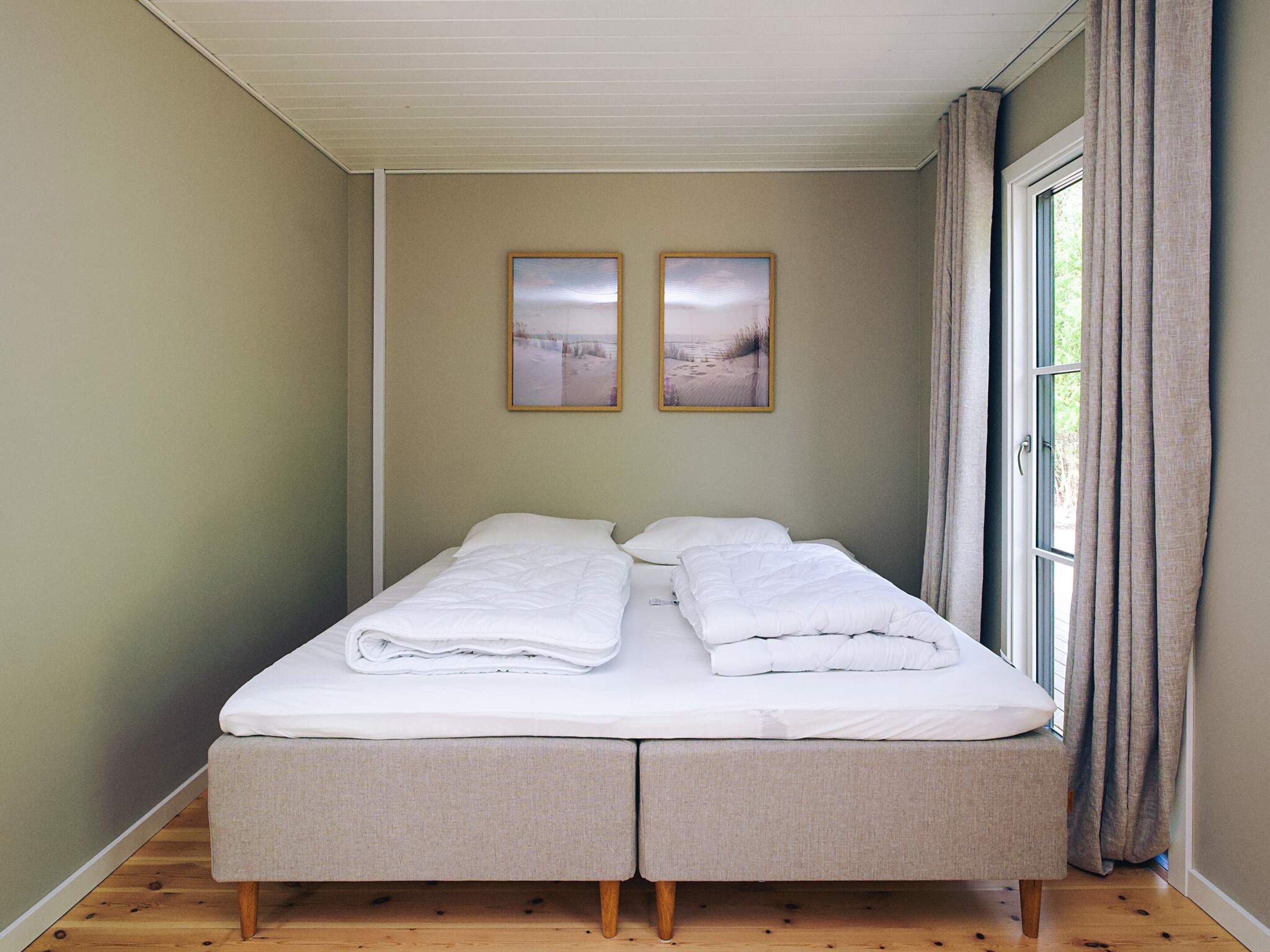 Ein Doppelbett mit weißen Leinentüchern, ein Fenster mit Vorhängen und zwei gerahmte Bilder an der Wand.