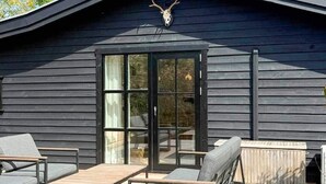 Un bâtiment moderne à l’extérieur sombre, doté d’une porte d’entrée en verre et d’un espace extérieur aménagé avec des coussins.