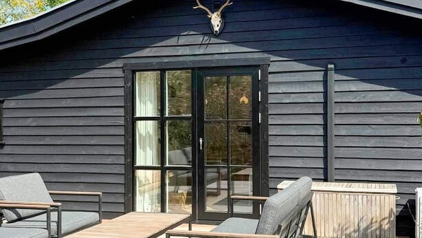 A modern building with a dark exterior, a glass door entrance, and outdoor seating with cushions. - 4 Star Holiday Home in Gilleleje (Gilleleje)