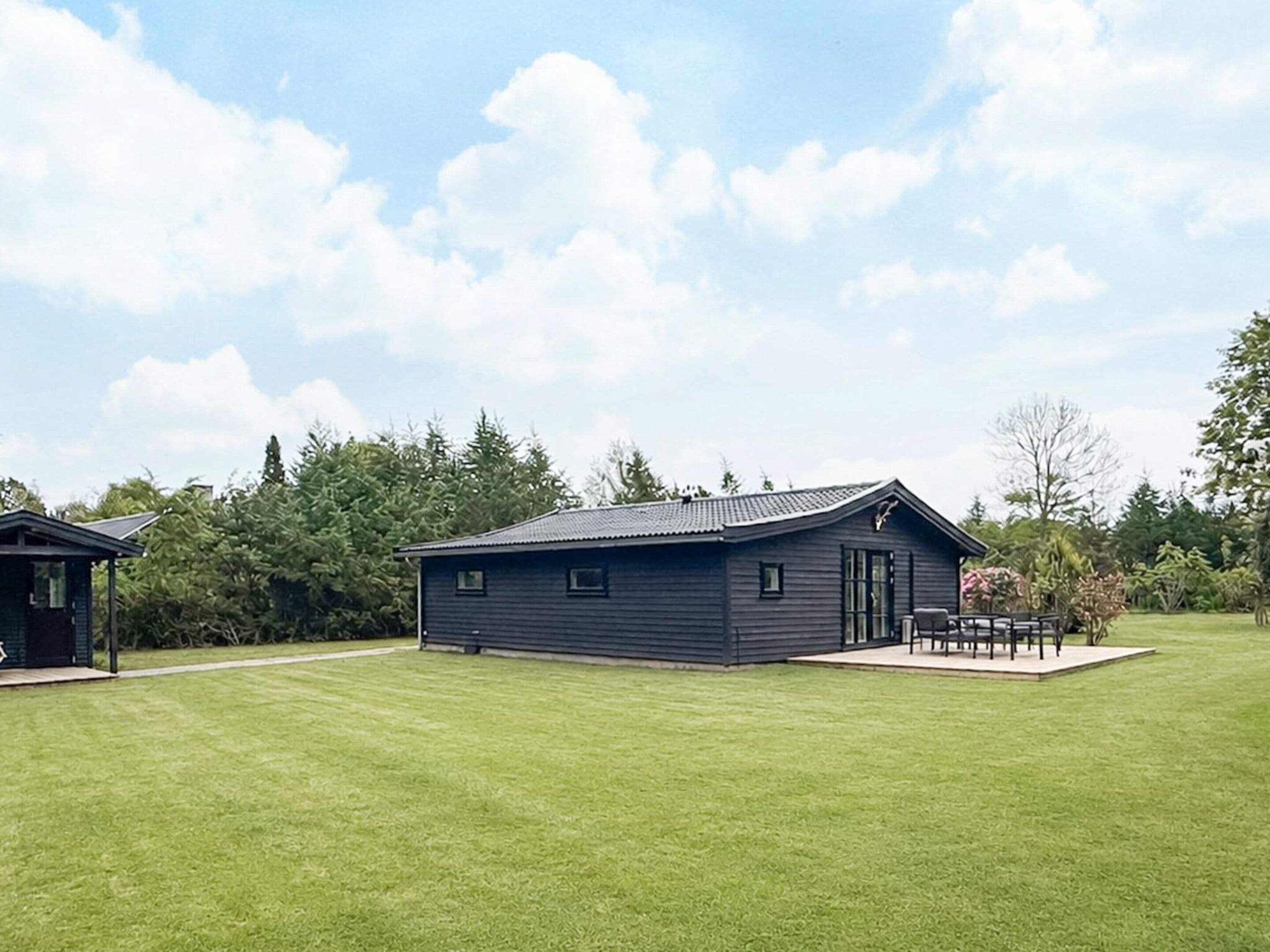 Een laag gebouw met een plat dak, een terras met een tafel en stoelen, en een verzorgd gazon.