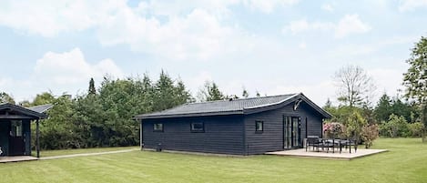 Een laag gebouw met een plat dak, een terras met een tafel en stoelen, en een verzorgd gazon.