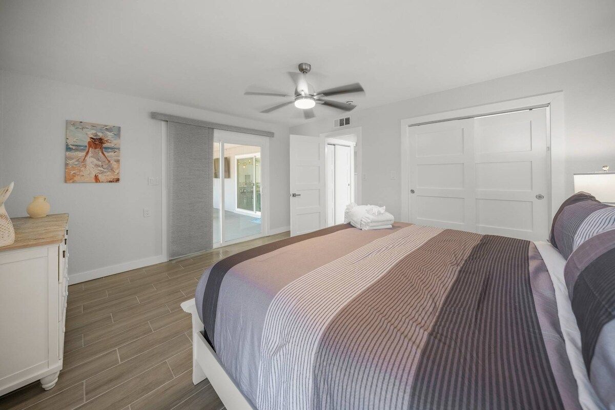 Une chambre à coucher avec un lit, un ventilateur de plafond, un tableau et une porte donnant sur un balcon.