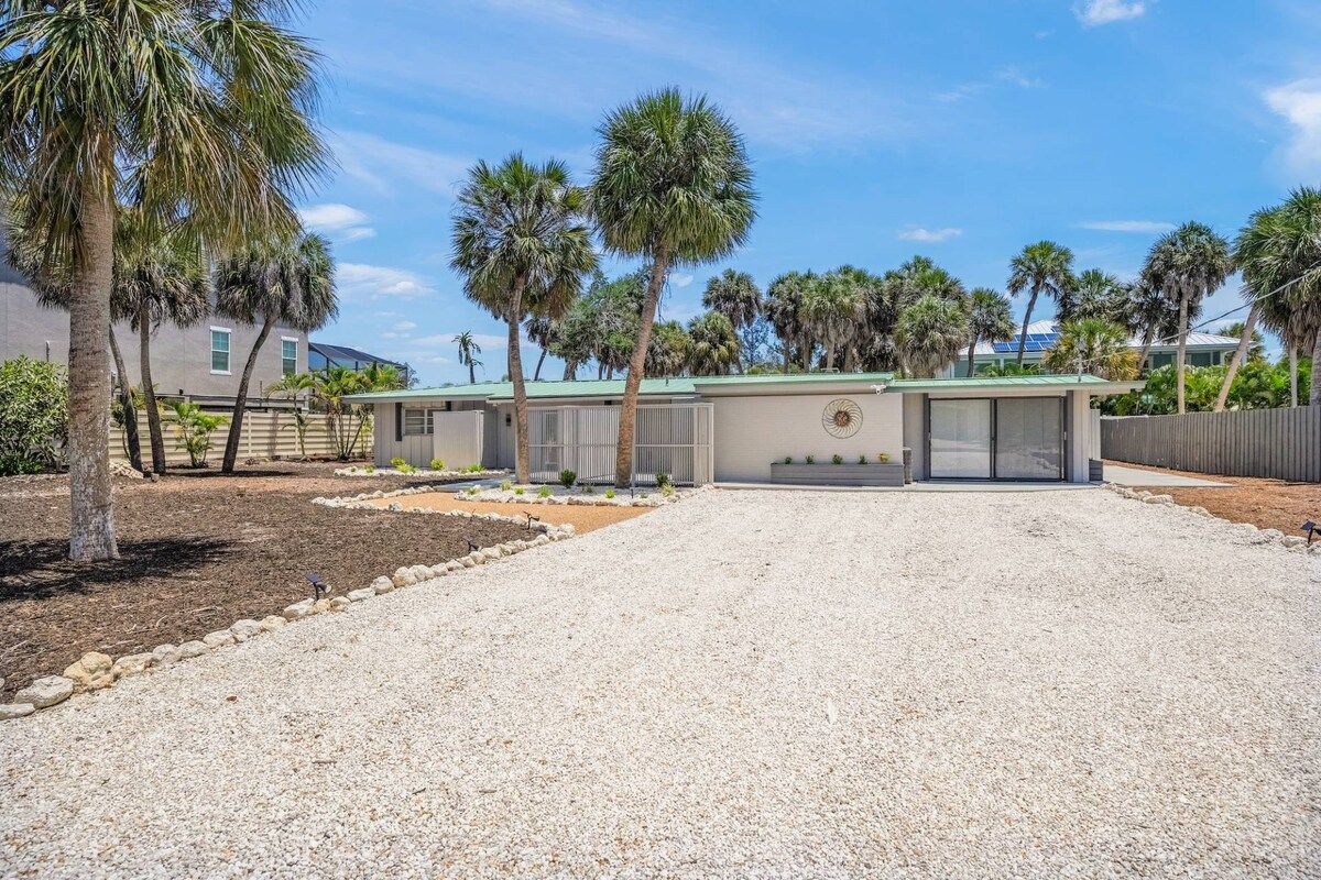 A residential property with a gravel driveway, palm trees, and a modern building with a green roof.