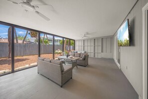 Eine geräumige Terrasse mit Deckenventilator, großem Fenster und an der Wand befestigtem Fernseher.