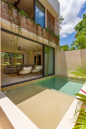 Ein modernes Haus mit Swimmingpool, einem Balkon mit Pflanzen und einem Wohnzimmer mit Sofa und Couchtisch.