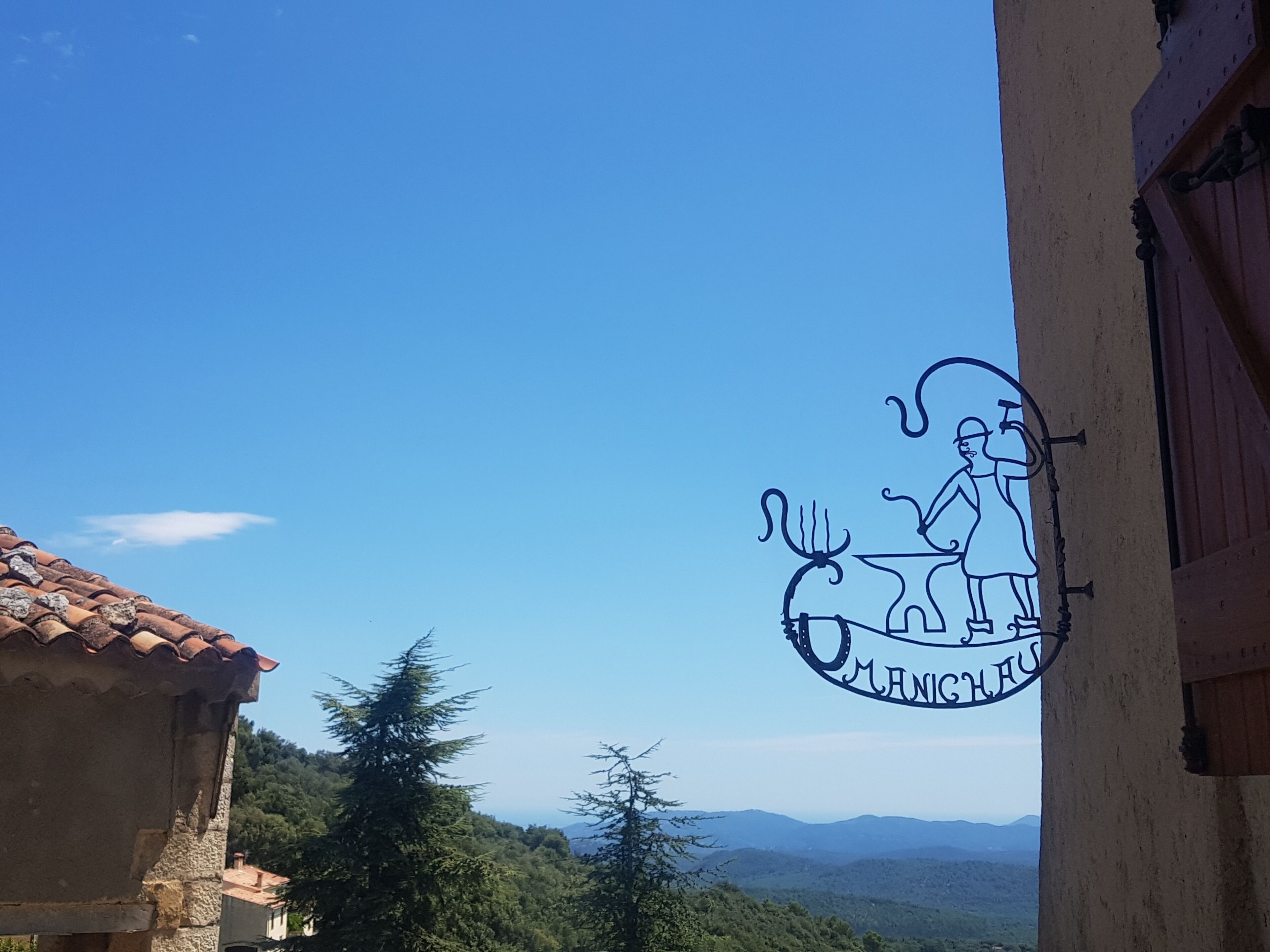 Un edificio con tejado de tejas, un cartel con un dibujo de una persona y un caballo, y vista de un paisaje boscoso.