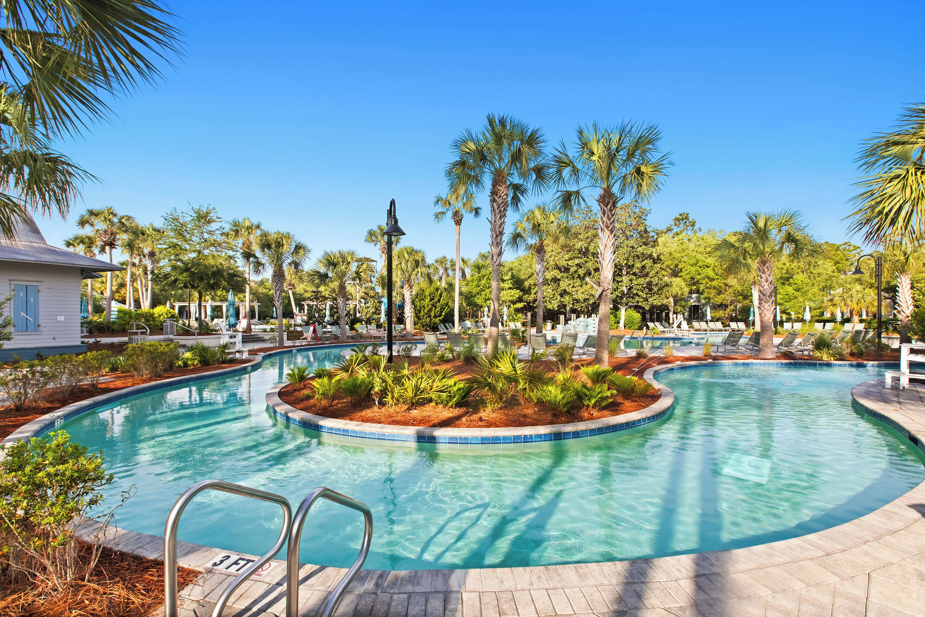 A sparkling lazy river winds through lush tropical landscaping under bright blue skies, inviting guests to float the day away in paradise.