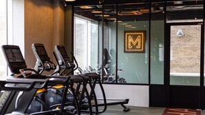 Ein Fitnessraum mit Trainingsrädern, einem sichtbaren Logo an der Wand und einer Backsteinmauer im Hintergrund.