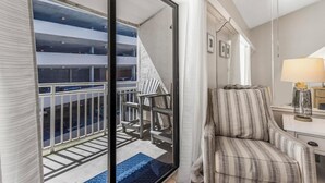 Ein Hotelzimmer mit Balkon, einem gestreiften Sessel, einer Lampe und Blick auf eine Parkgarage.