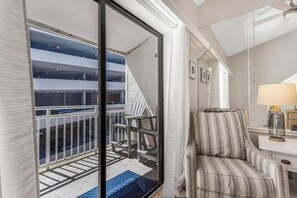 Ein Hotelzimmer mit Balkon, einem gestreiften Sessel, einer Lampe und Blick auf eine Parkgarage.