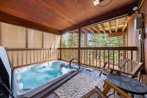 A wooden deck with a hot tub, outdoor seating, and a view of trees. - 5 mins to Beach • AC & Hot Tub • Game Room  • EV Charger (Kings Beach)