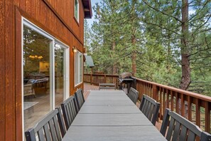 A wooden deck with a table and chairs, surrounded by trees. - 5 mins to Beach • AC & Hot Tub • Game Room  • EV Charger (Kings Beach)