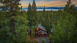 A cabin surrounded by dense forest with a view of a lake and mountains in the background. - 5 mins to Beach • AC & Hot Tub • Game Room  • EV Charger (Kings Beach)