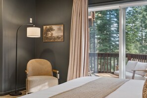 Habitación de hotel con cama, una silla, una lámpara de pie, un cuadro y vista a árboles desde un balcón.