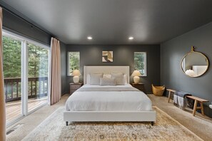 A bedroom with a large bed, two bedside tables, a round mirror, a bench, and a view of the outdoors. - 5 mins to Beach • AC & Hot Tub • Game Room  • EV Charger (Kings Beach)