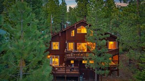 A multi-story wooden cabin with balconies, surrounded by dense forest. - 5 mins to Beach • AC & Hot Tub • Game Room  • EV Charger (Kings Beach)
