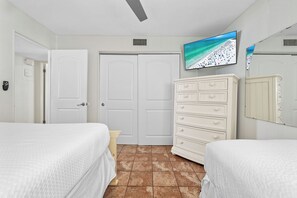 Ein Hotelzimmer mit zwei Betten, einem Schminktisch, einem an der Wand befestigten Fernseher und einer Tür.