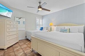 Ein Schlafzimmer mit einem Bett, zwei Nachttischen, einer Kommode, einem Deckenventilator und einem an der Wand befestigten Fernseher.