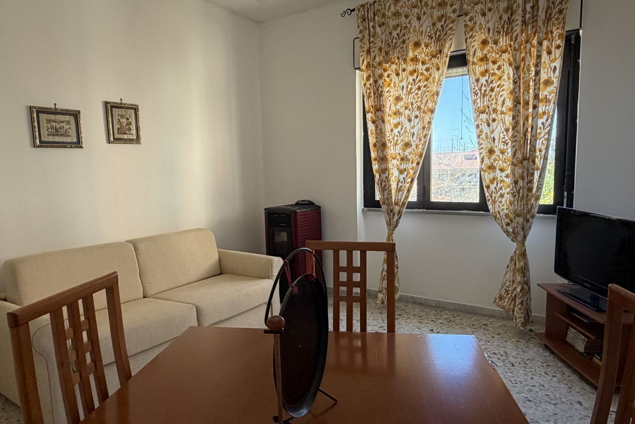 Un soggiorno con divano, tavolo da pranzo con sedie, televisore e due quadri appesi al muro.