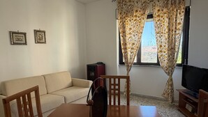 A living room with a sofa, a dining table with chairs, a television, and two framed pictures on the wall. - Kairos - Casa Vacanze (Fuscaldo)