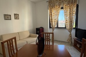 Una sala de estar con un sofá, una mesa de comedor con sillas, un televisor y dos cuadros en la pared.