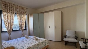 A bedroom with a bed, a wardrobe, a chair, and a window with curtains. - Kairos - Casa Vacanze (Fuscaldo)