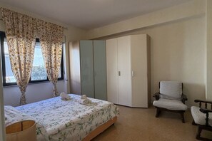 Un dormitorio con cama, armario, silla y ventana con cortinas.