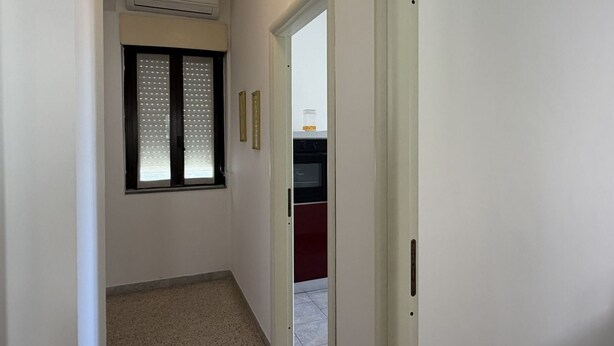 A narrow hallway with a window, an air conditioning unit, and a door leading to a kitchen area. - Kairos - Casa Vacanze (Fuscaldo)